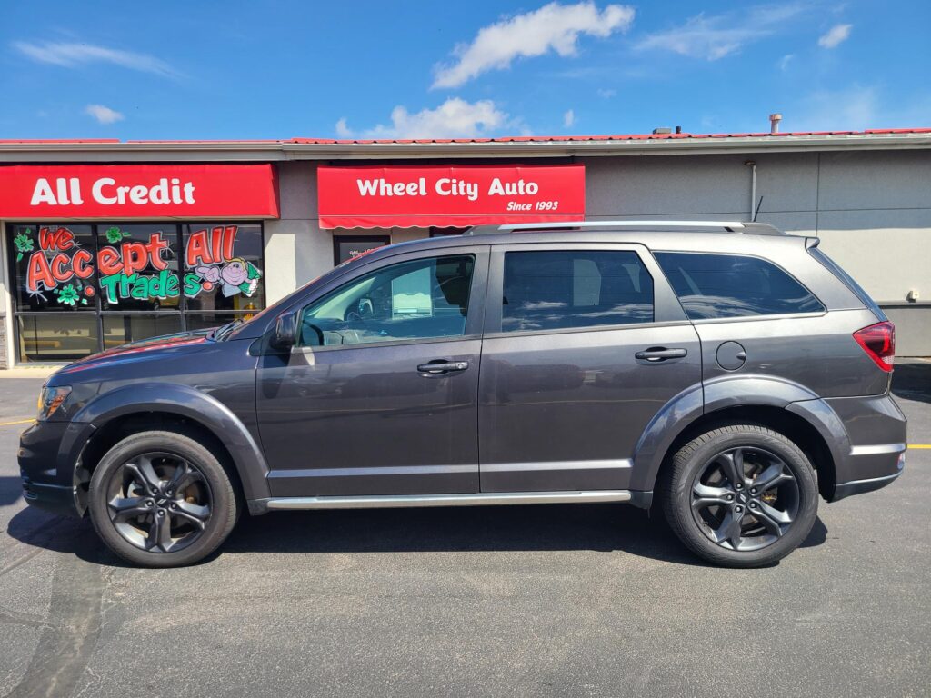 Front of a car dealership with red signs saying 'All Credit' and 'Wheel City Auto' and a gray SUV parked in front.