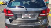 Rear view of a dark gray Dodge Journey Crossroad SUV with a Wheel City Auto Finance Centers license plate frame visible, parked in a dealership lot with other cars and a red 'We Finance' sign in the background.