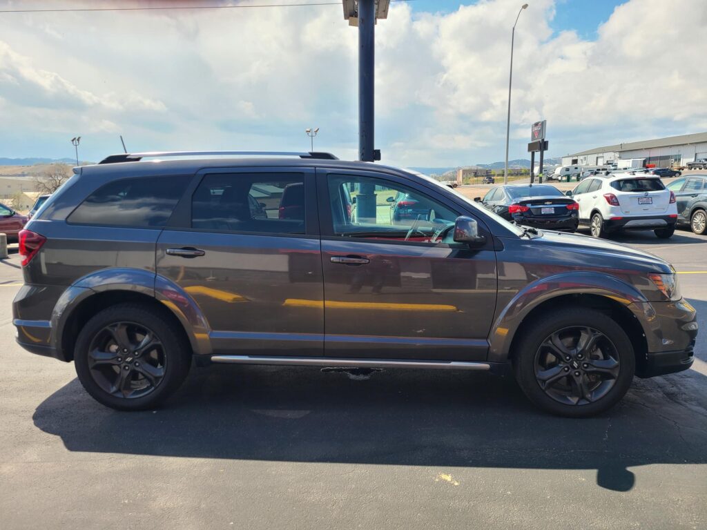 Side view of a dark gray SUV parked in a lot with other cars and a dealership in the background under a cloudy sky