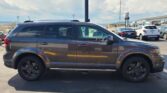 Side view of a dark gray SUV parked in a lot with other cars and a dealership in the background under a cloudy sky