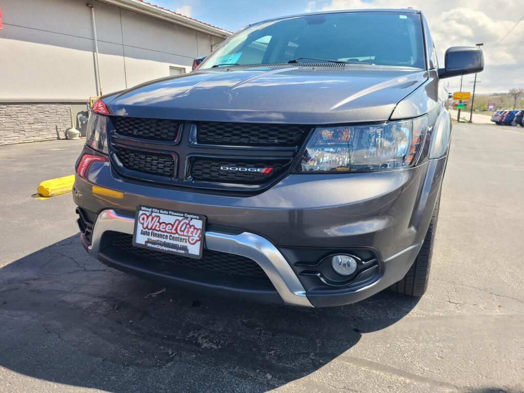 Close-up of a dark gray Dodge SUV parked outdoors, showing front grille and headlights with a Wheel City dealer plate in the foreground.