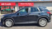 Front view of a car dealership with red signs reading 'Wheel City Auto' and 'All Credit'; a dark SUV is parked in front of the store.