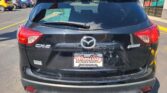 Rear view of a black Mazda CX-5 at a car lot with a green dealership window sticker on the rear windshield and Wheel City Auto Finance Centers license plate frame visible.