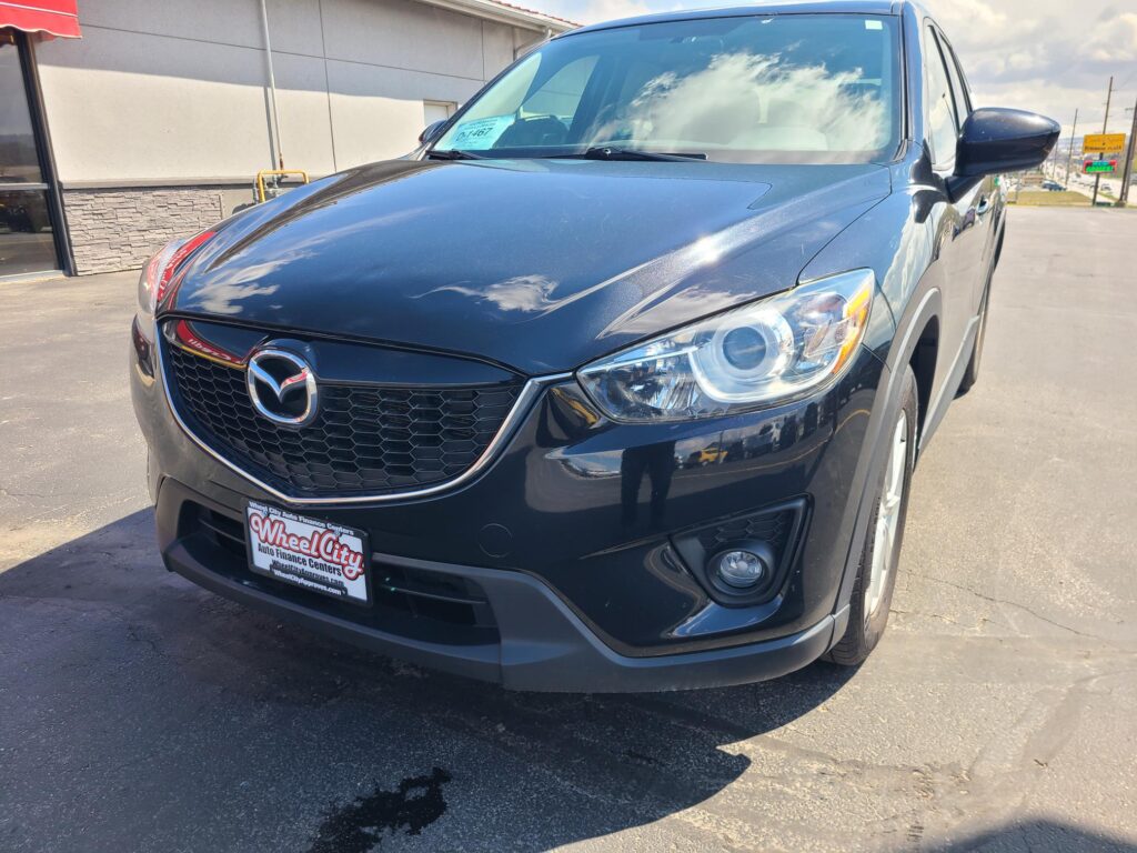 Front view of a dark blue Mazda SUV parked at a dealership, Wheel City plate frame visible in the foreground