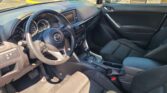 Interior of a Mazda car from the driver's seat showing steering wheel, dashboard, and center console with gear shifter and touchscreen display.