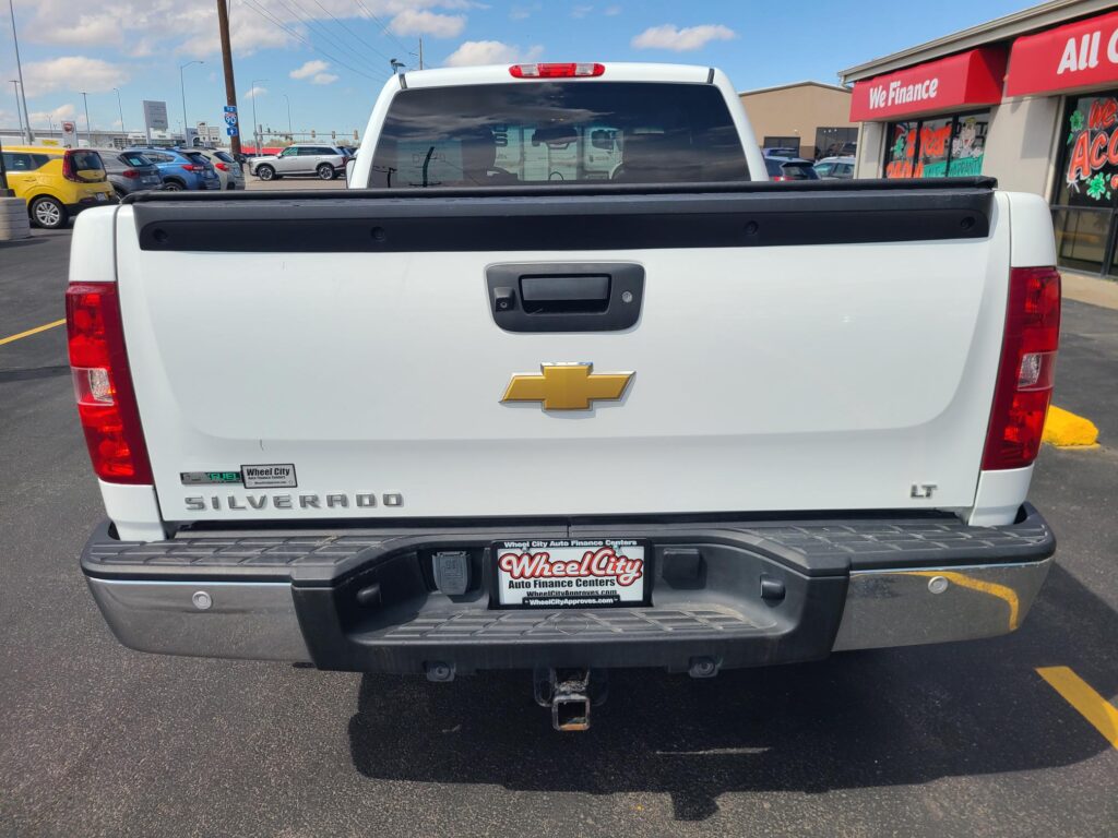 Rear view of a white Chevrolet Silverado LT pickup in a car dealership lot, showing the tailgate, Chevrolet emblem, and tow hitch.