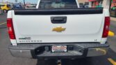 Rear view of a white Chevrolet Silverado LT pickup in a car dealership lot, showing the tailgate, Chevrolet emblem, and tow hitch.