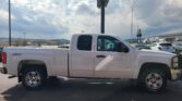 White Chevrolet Silverado pickup parked in a lot with yellow parking blocks and a cloudy blue sky above.