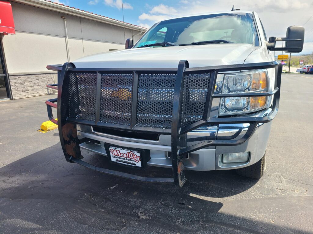 Front view of a white pickup truck with a large black mesh grille guard in a parking lot