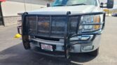 Front view of a white pickup truck with a large black mesh grille guard in a parking lot