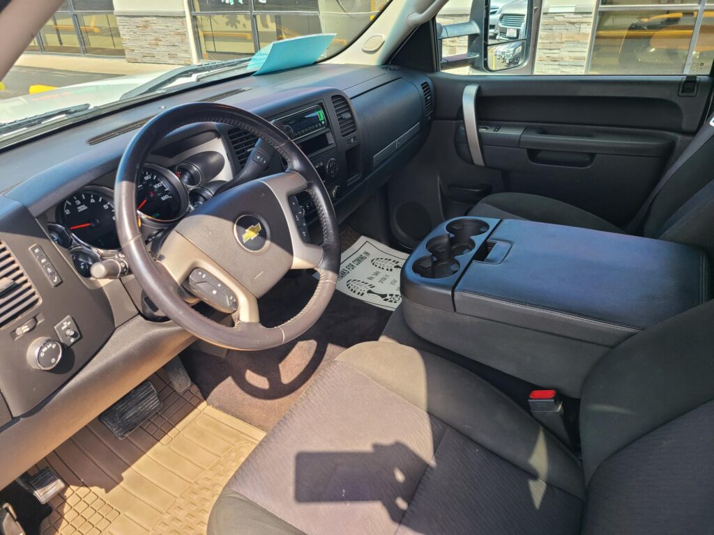Interior of a Chevrolet pickup: steering wheel, dashboard, and center console with cup holders in view; blue paper on the dashboard
