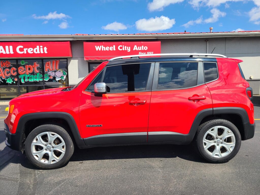 Red Jeep Renegade parked in front of Wheel City Auto storefront under a sunny, blue sky.