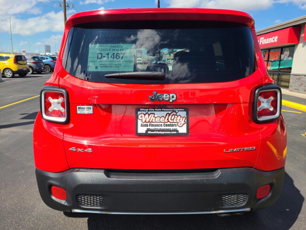 Rear view of a red Jeep SUV in a dealership lot, showing tail lights, 4x4 and Limited badges, and a Wheel City Auto Finance Centers plate on the back.