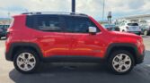 Red Jeep Renegade parked in a lot, side view showing doors, wheels, and roof rails with other cars and a dealership in the background.