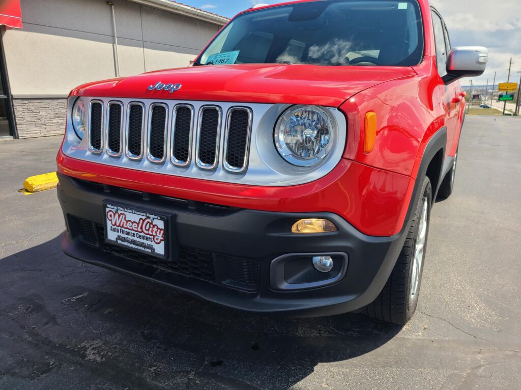 Red Jeep SUV front view showing the chrome seven-slot grille and round headlight at a dealership lot.