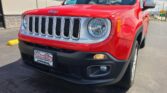 Red Jeep SUV front view showing the chrome seven-slot grille and round headlight at a dealership lot.