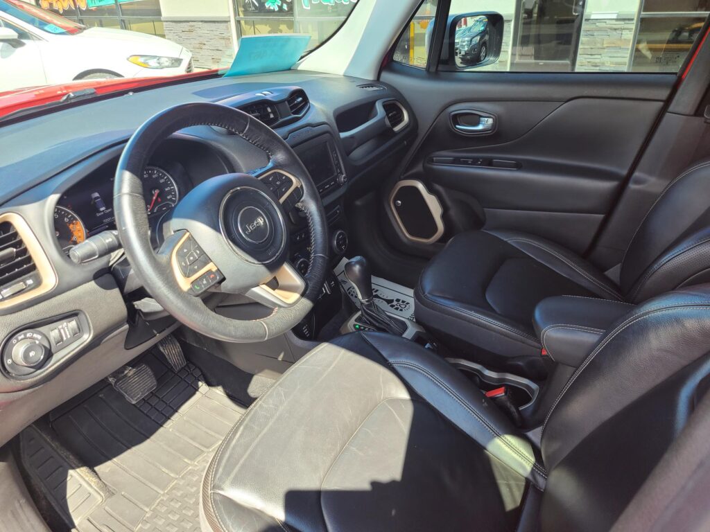 Front interior of a Jeep SUV: black leather seats, steering wheel with Jeep emblem, center console screen, and gear shifter visible in daylight.