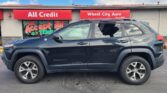 Blue SUV parked in front of a red-sign auto dealership with 'All Credit' and 'Wheel City Auto' storefront signs.
