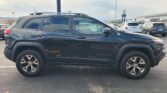 Black Jeep Cherokee SUV parked in a parking lot with other cars and an industrial building in the background.