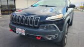 Front-quarter view of a dark gray Jeep SUV parked outside a Wheel City Auto dealership with a red canopy sign says 'Since 1993'