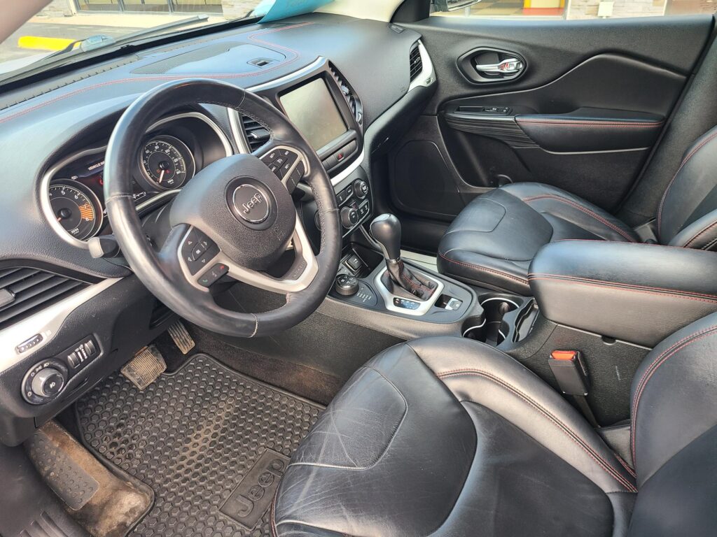 Interior of a black leather Jeep cabin with red contrast stitching, steering wheel, center touchscreen, gear shifter, and front seats visible.