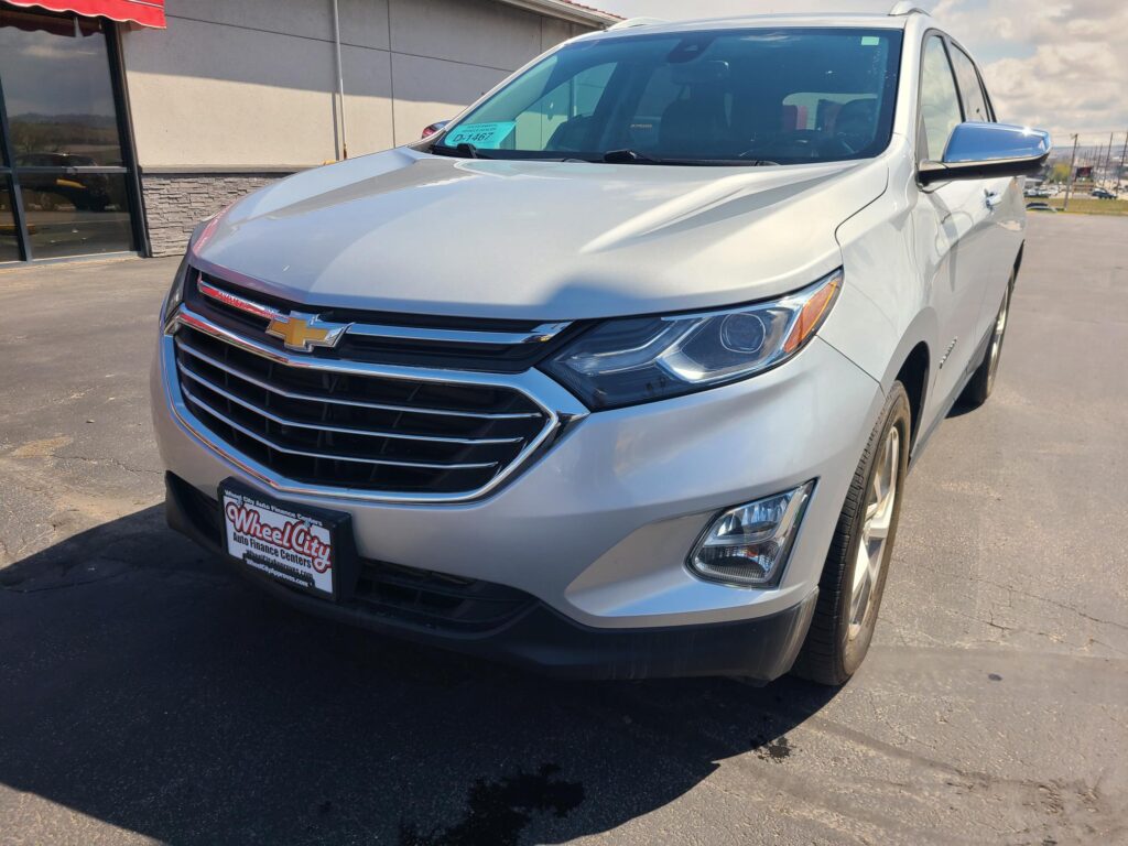 Silver Chevrolet SUV parked outdoors at a dealership, front view showing grille and headlights, Wheel City license plate frame visible.