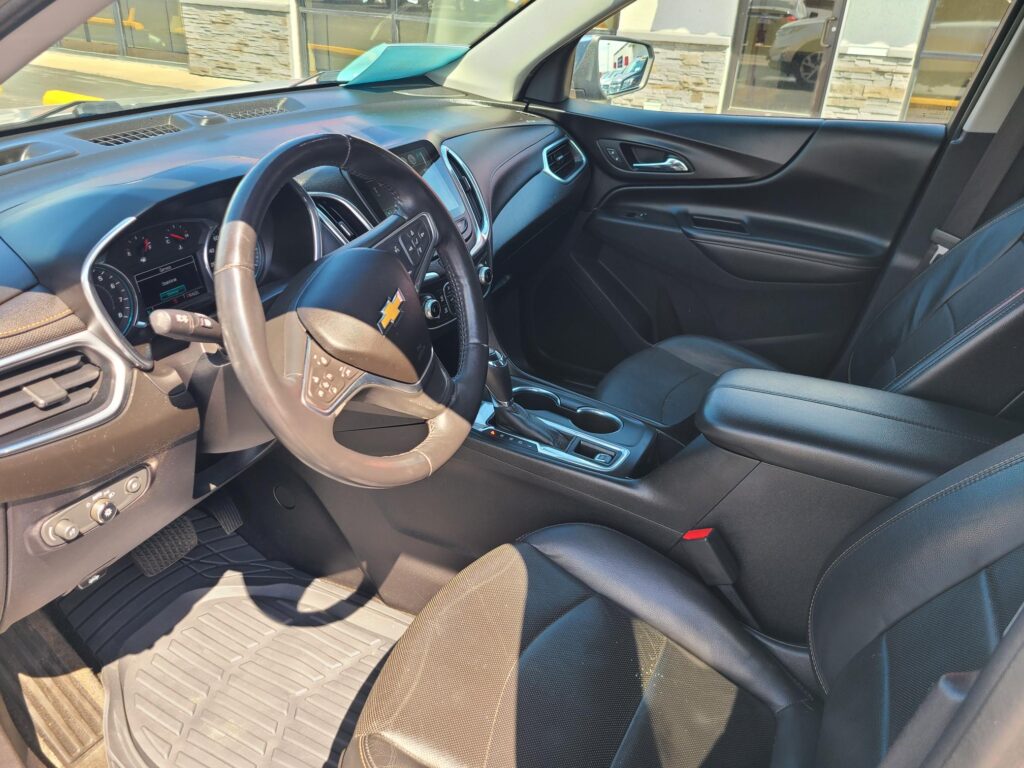 Front interior of a black Chevrolet SUV, showing the steering wheel, center touchscreen, and dark leather seats inside the cabin.