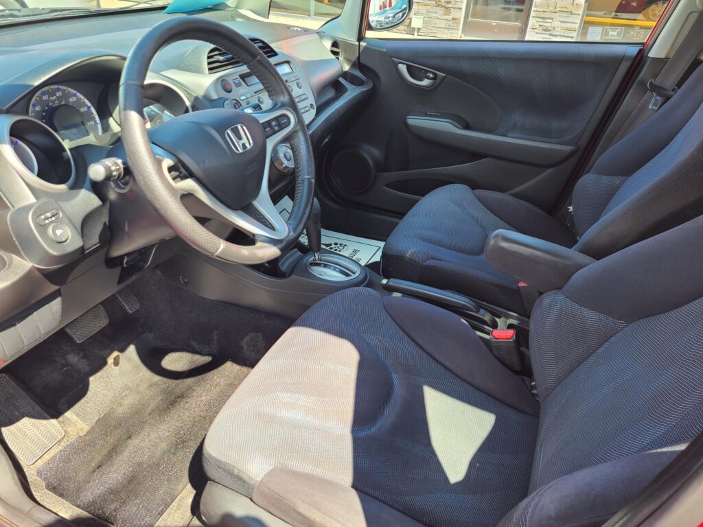 Interior of a Honda car from the driver's side showing the steering wheel, dashboard with controls, gear shifter, and front seats.