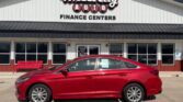 Red sedan parked in front of Wheel City Auto Finance Centers storefront on a sunny day.