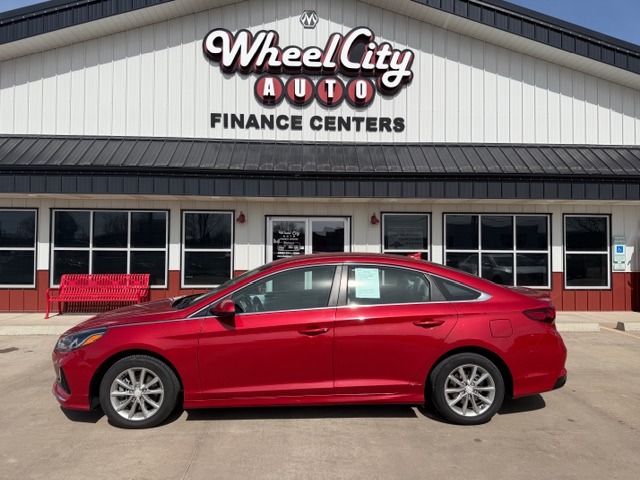 Red sedan parked in front of Wheel City Auto Finance Centers storefront on a sunny day.