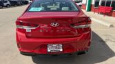Rear view of a red Hyundai Sonata parked in a dealership lot, showing S E badge and license plate frame reading 'Wheel City'