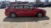 Red four-door sedan parked in a parking lot, viewed from the side.