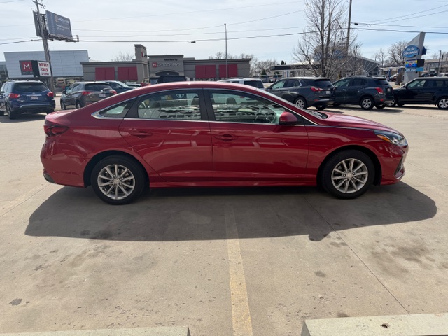 Red four-door sedan parked in a parking lot, viewed from the side.