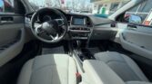 Interior of a light-gray Hyundai sedan: steering wheel, center touchscreen, climate controls, and front seats.
