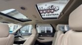 Beige leather car interior with a panoramic sunroof; dealership building visible through the sunroof opening.