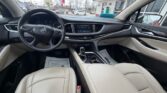 Interior of a beige-leather Buick car, view from the back seat showing steering wheel, center console with touchscreen, gear shifter, and front seats.