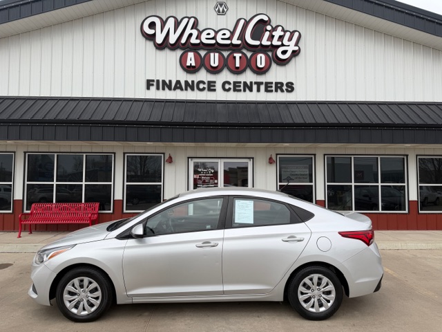 Silver sedan parked in front of Wheel City Auto Finance Centers storefront with large logo sign above the entrance (car dealership scene)