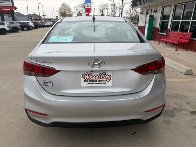 Rear view of a white Hyundai Sonata at a car dealership; blue window sticker on the rear windshield and Wheel City Auto Finance Centers plate.
