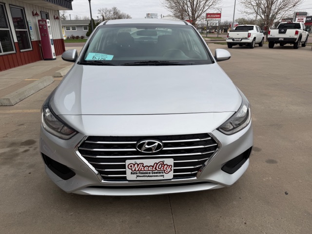 Front view of a silver Hyundai sedan parked in a dealership lot, with a Wheel City license plate frame and a blue windshield sticker visible on the driver's side of the windshield.
