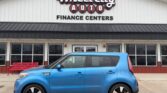 Blue compact car parked in front of Wheel City Auto Finance Centers storefront, dealership sign visible above.