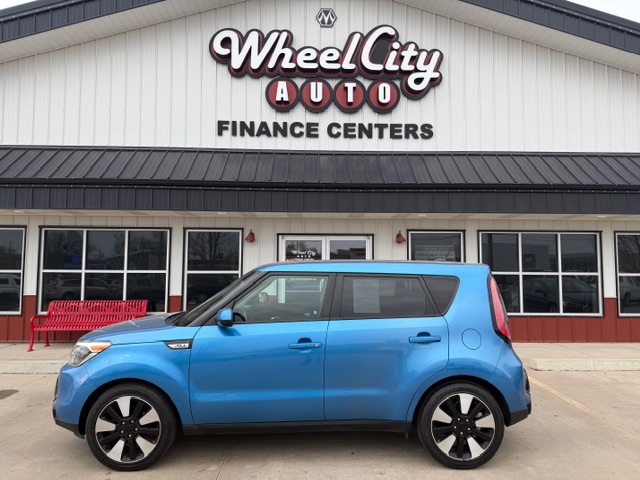 Blue compact car parked in front of Wheel City Auto Finance Centers storefront, dealership sign visible above.
