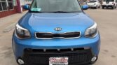Front view of a blue Kia SUV parked in a dealership lot, showing the grille, headlights, and a Wheel City Auto Finance Centers license plate.