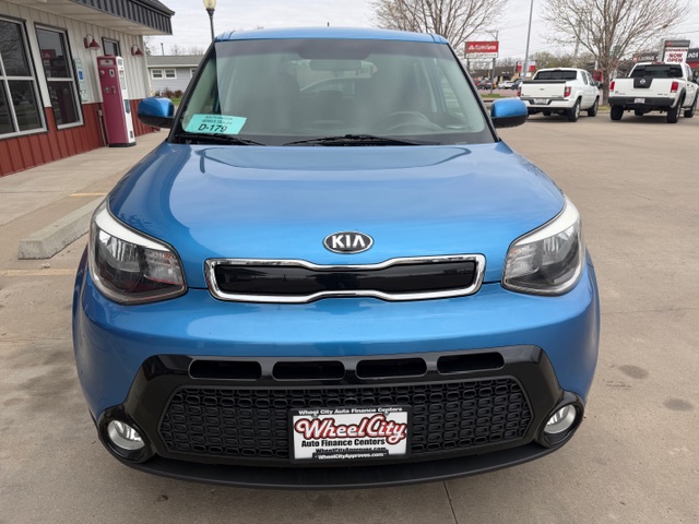 Front view of a blue Kia SUV parked in a dealership lot, showing the grille, headlights, and a Wheel City Auto Finance Centers license plate.