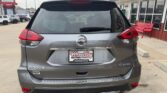Gray Nissan Rogue SUV parked outside a dealership; rear view with Wheel City license plate frame, Rogue badge left, SV AWD badge right, red taillights.