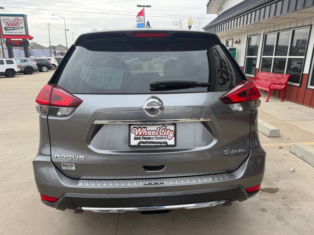 Gray Nissan Rogue SUV parked outside a dealership; rear view with Wheel City license plate frame, Rogue badge left, SV AWD badge right, red taillights.