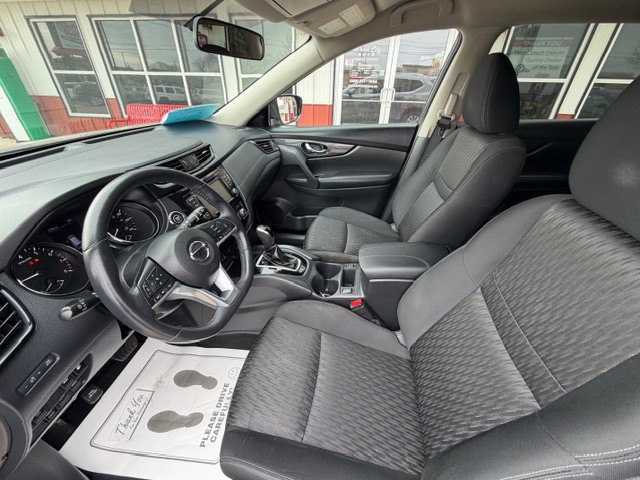 Inside a modern sedan showing the driver's seat and front passenger seat, with a steering wheel, dashboard, and center console including a gear shift; showroom floor mat visible on the floor.