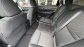 Rear passenger area of a car showing two outer seats and a middle seat with seat belts, black fabric upholstery, and headrests; front seats partially visible.