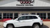 White Jeep Cherokee SUV parked in front of Wheel City Auto Finance Centers storefront with red bench and large sign on the building