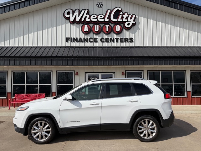White Jeep Cherokee SUV parked in front of Wheel City Auto Finance Centers storefront with red bench and large sign on the building