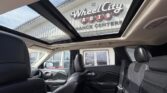 Interior of a black leather SUV with a panoramic sunroof; dealership storefront visible through the glass roof at Wheel City Auto.